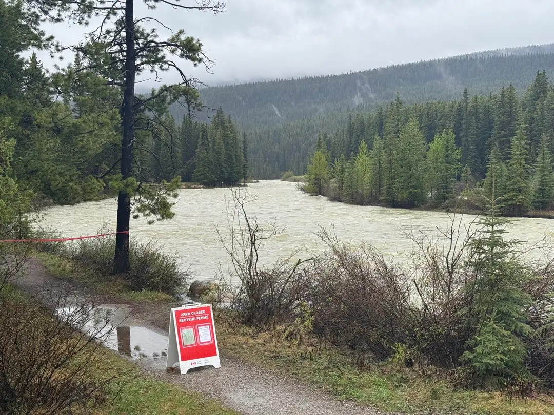 Area closed sign beside a wet trail with a high, swollen river in the background.
