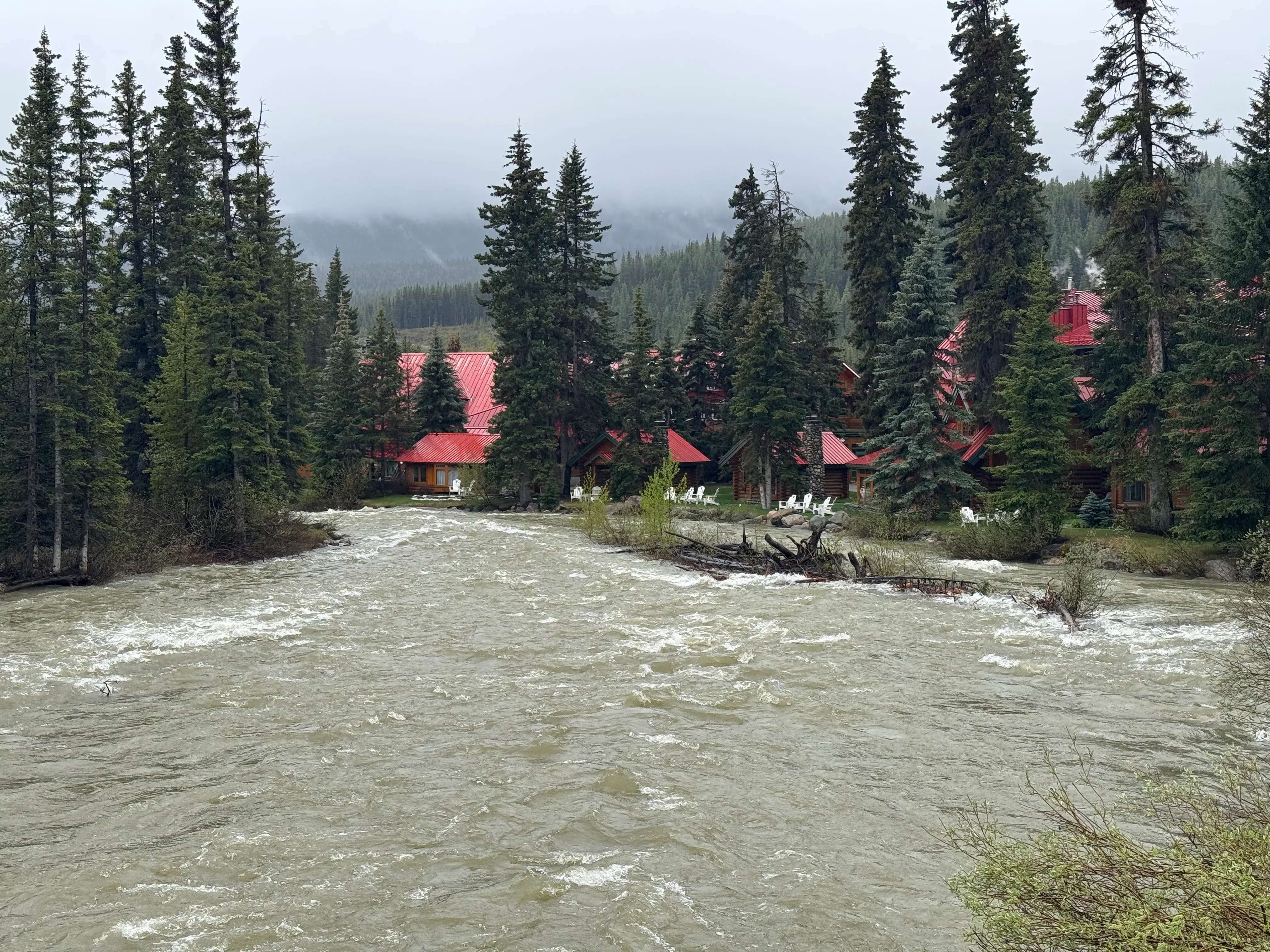 High, silty river water flowing through the Post Hotel area in Lake Louise, with buildings set back from the river.