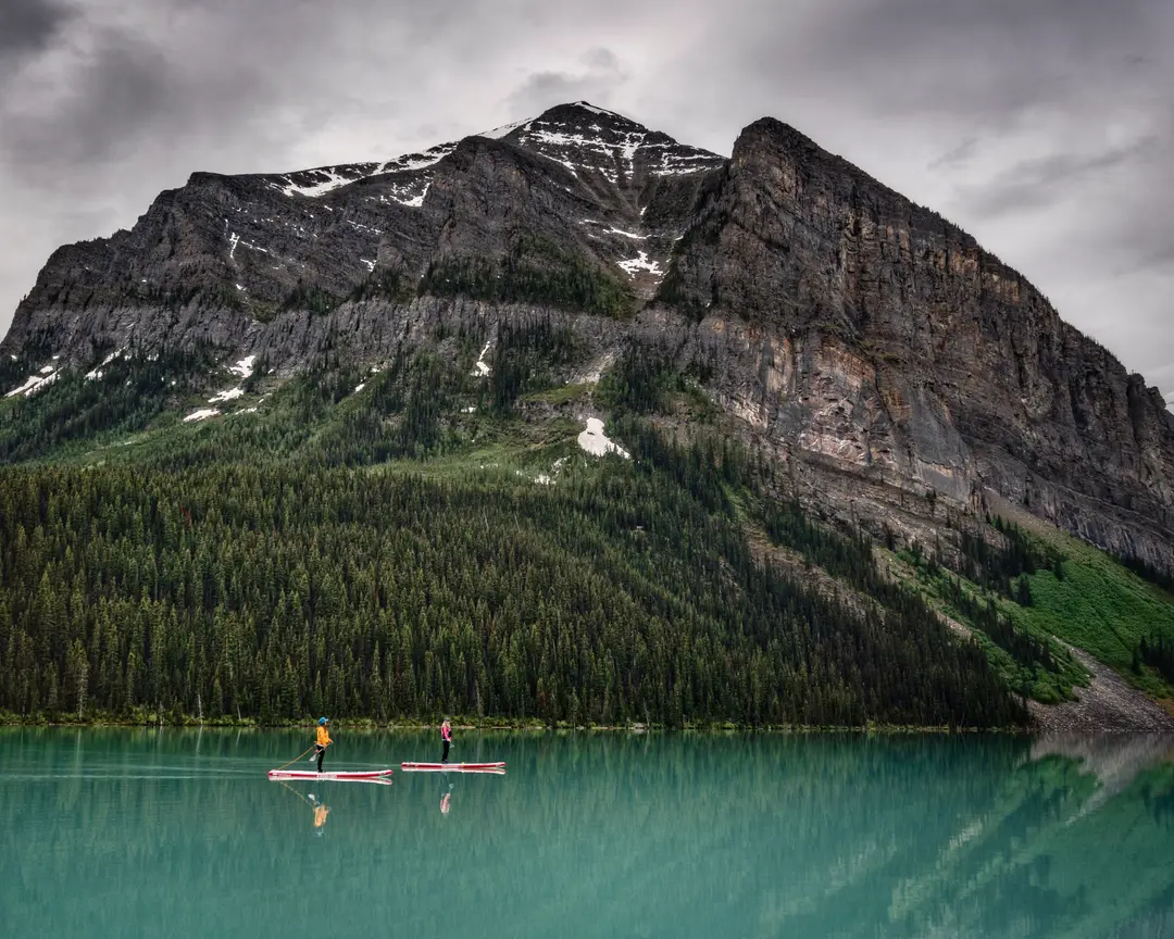 Two paddleboarders on the turquoise water of Lake Louise with Fairview Mountain rising above the far shore.