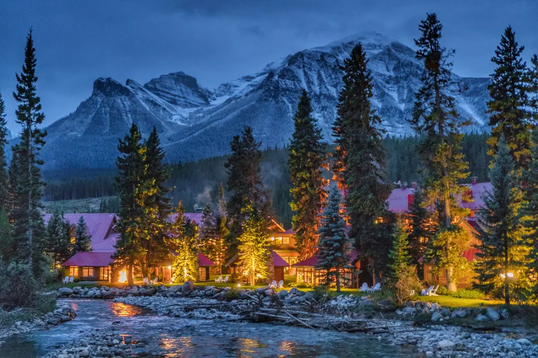 The Post Hotel lit at dusk beside the Pipestone River in fall.
